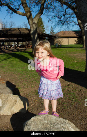 Young Caucasian girl playing in the park. She is wearing a pink t-shirt and blue skirt. Stock Photo