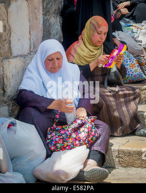 Two Israeli Arab woman sitting next to a bus stop waiting for a ride home near the old city of Jerusalem, Israel Stock Photo