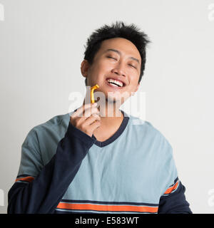 Asian male shaving his beard in a morning, on plain background Stock Photo