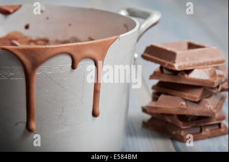 dirt pan with hot melted chocolate dripping and chocolate blocks, on wooden table Stock Photo