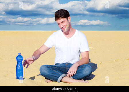 Handsome man reaching for a bottle of water in desert Stock Photo