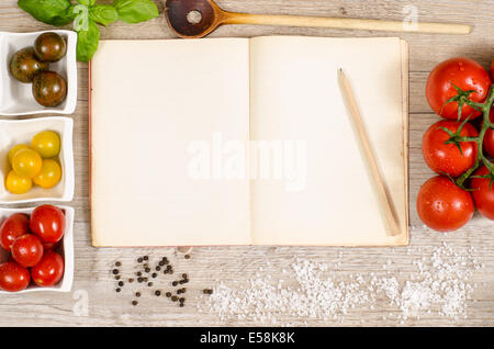 Old book with advertising space and pencil, wooden spoon, pepper, salt and tomatoes Stock Photo