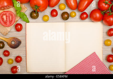 Different tomatoes, basil, wooden spoon, napkin and a recipe book with text space Stock Photo