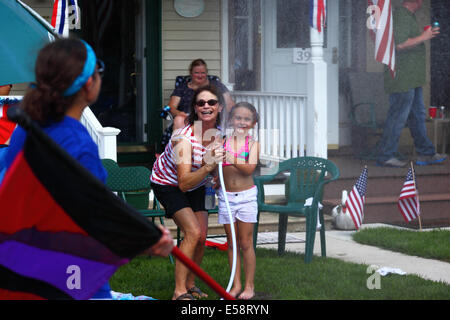 Girl and her mother playing with hosepipe in front of porch on 4th of July Independence Day public holiday, Catonsville, Maryland, USA Stock Photo