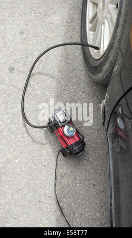 Portable air compressor putting air in a front tire while connected to the power outlet in the car. Stock Photo