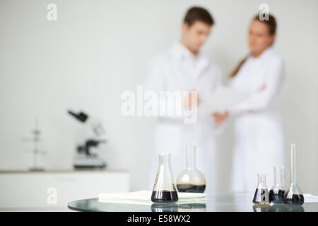 Test-tubes with liquid oil on background of two scientists working in laboratory Stock Photo