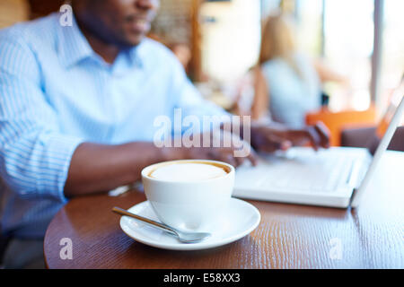 Image of cup of latte on background of man typing on laptop in cafe Stock Photo