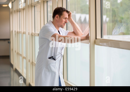 Male doctor standing in hospital looking out of window Stock Photo