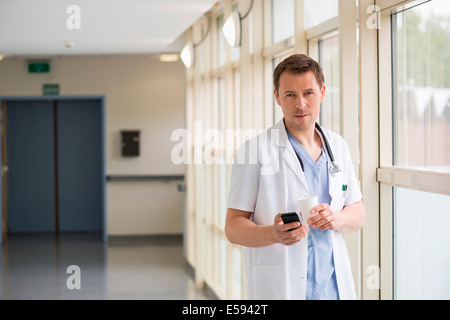 Male doctor messaging on a mobile phone while drinking coffee Stock Photo
