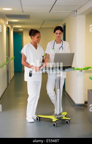 Female doctor and nurse using laptop in hospital corridor