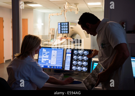 Doctors examining scan on computer with patient on MRI scanner in background Stock Photo
