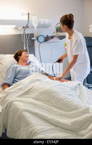 Female nurse checking patient's blood pressure on hospital bed Stock Photo