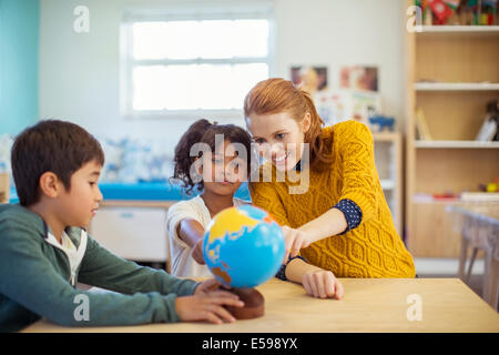 Students and teacher examining globe in classroom Stock Photo
