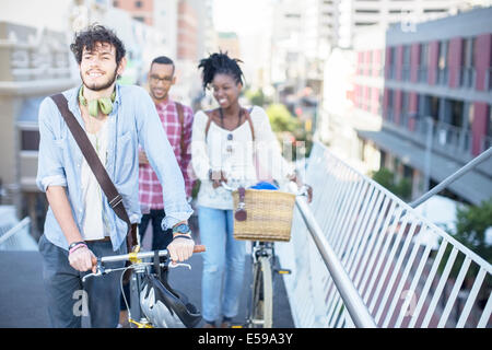 Friends pushing bicycles on city street Stock Photo
