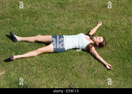 Young woman wearing a mini skirt laying on grass with arms and legs outstretched Stock Photo