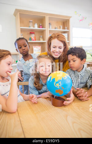 Students and teacher examining globe in classroom Stock Photo