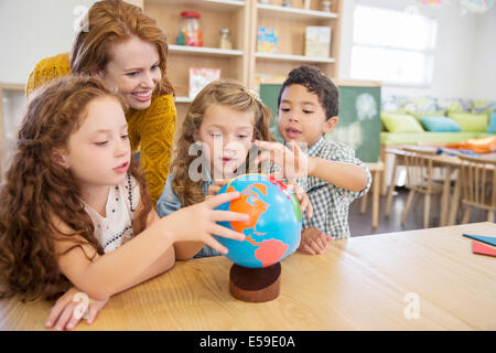 Students and teacher examining globe in classroom Stock Photo