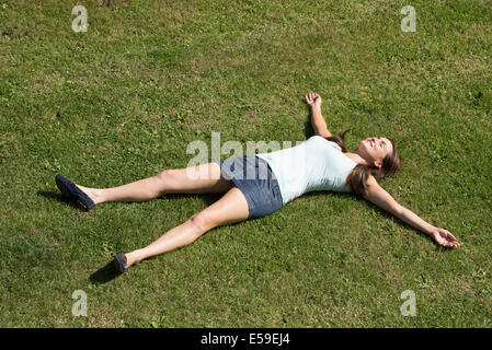 Young woman wearing a mini skirt laying on grass with arms and legs outstretched Stock Photo