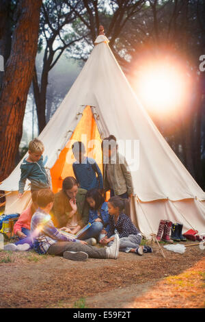 Students and teacher reading at teepee at campsite