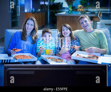 Family eating pizza in front of television in living room Stock Photo