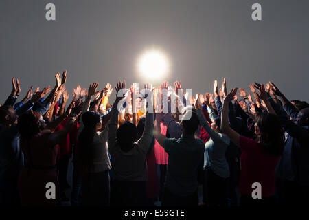 Diverse crowd with arms raised around bright light Stock Photo