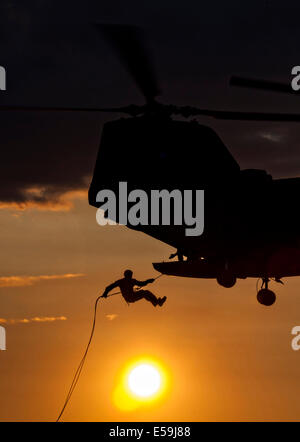 A US Marine commando with the 4th Reconnaissance Battalion is silhouetted by the setting sun as he rappels out of a CH-46E Sea Knight helicopter at Camp Upshur July 17, 2014 in Quantico, Virginia. Stock Photo