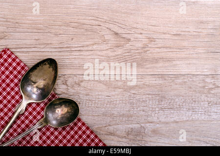 Two old silver spoons on checkered cloth and weathered wood Stock Photo
