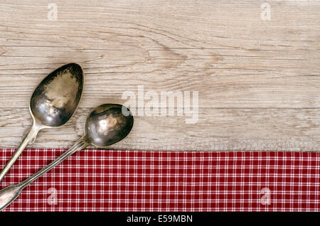Weathered wood with two silver spoons on a red and white checkered cloth Stock Photo