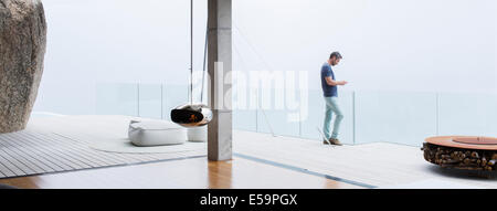 Man using cell phone on balcony of modern house Stock Photo