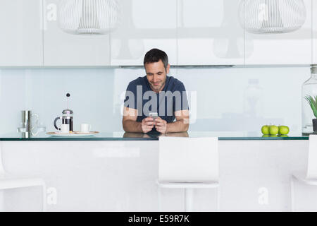 Man using cell phone in modern kitchen Stock Photo