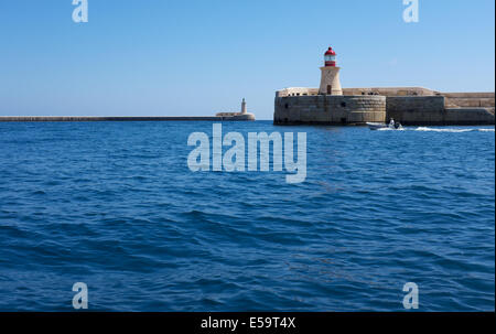 St Elmo Lighthouse & Breakwater Left with Ricosoli East Breakwater & Ricosoli Lighthouse foreground with small boat passing Stock Photo