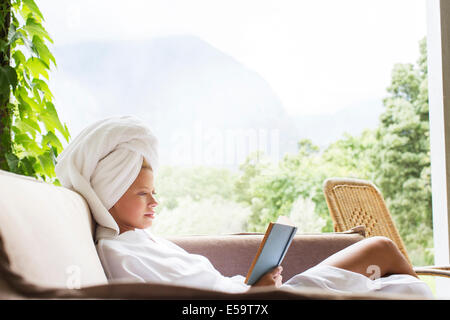 Woman in bathrobe reading on sofa