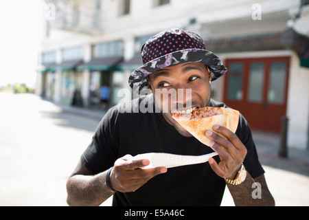 African American man eating pizza on city street Stock Photo