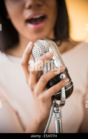 Mixed race woman singing into vintage microphone Stock Photo