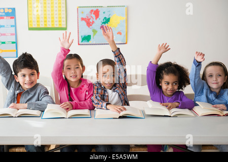 Students raising hands in classroom Stock Photo