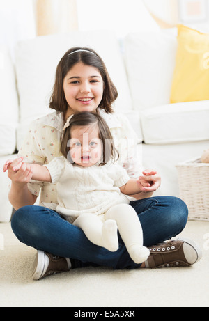 Hispanic girl holding toddler sister in living room Stock Photo