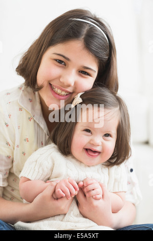 Hispanic girl holding toddler sister in living room Stock Photo