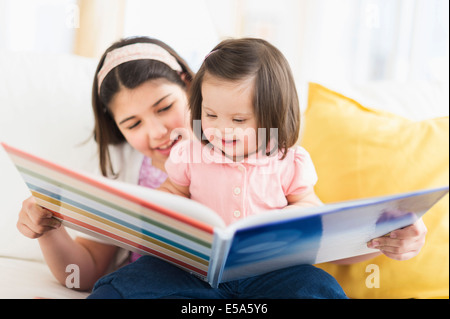 Hispanic girl reading to toddler sister in living room Stock Photo