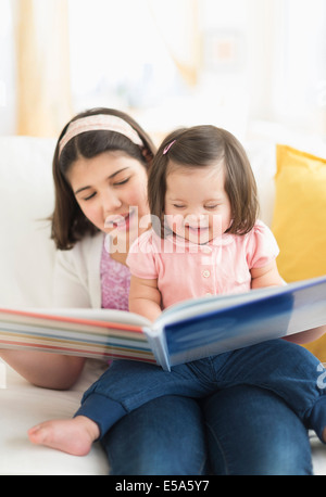 Hispanic girl reading to toddler sister in living room Stock Photo