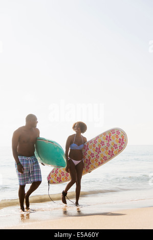 Couple carrying surfboards on beach Stock Photo