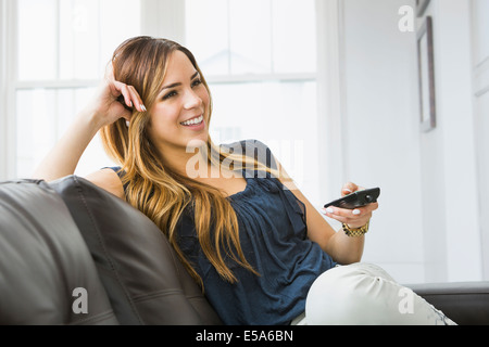 Mixed race woman watching television on sofa Stock Photo