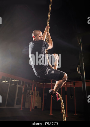 Hispanic man climbing rope in gym Stock Photo