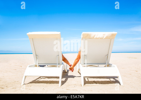 Couple holding hands in lounge chairs on beach Stock Photo