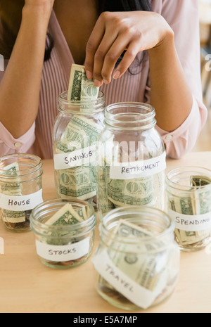 Mixed race woman putting money in savings jars Stock Photo