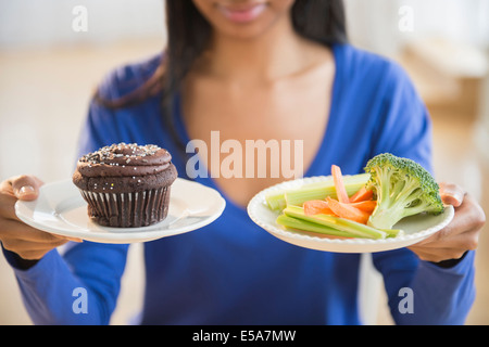 Mixed race woman choosing vegetables or cupcake Stock Photo