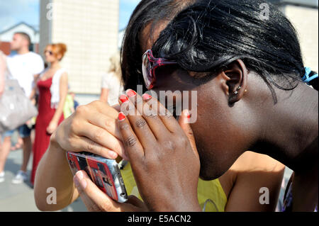 Two young woman looking at screen on smart phone, shielding screen from sun with hands, UK Stock Photo