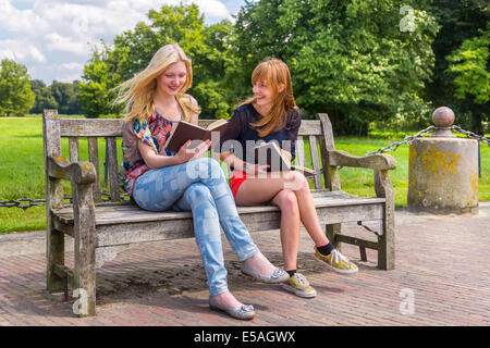 Girls sitting on wooden bench in park reading books Stock Photo
