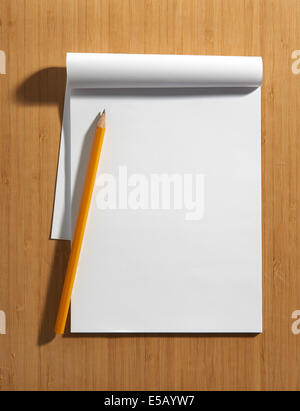 Overhead view of a blank white page of a notepad with copy space and a pencil lying on a wooden surface Stock Photo