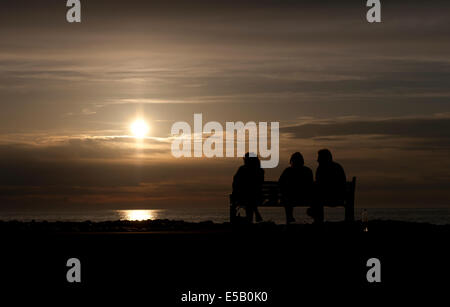 Aberaeron , Cardigan Bay, West Wales, Wales, UK; 3 people sitting on bence on harbour wall enjoying the sunset. Stock Photo