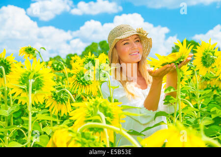 Portrait of cute girl in sunflowers field, holding in hands one big yellow flower, bright sunny day, summer holidays, enjoying c Stock Photo